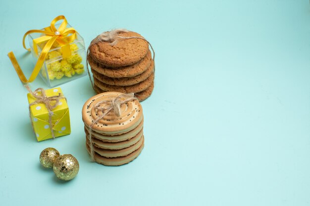 파스텔 녹색 배경의 오른쪽에 있는 장식 액세서리 옆에 쌓인 다양한 맛있는 쿠키와 아름다운 노란색 선물 상자가 있는 xsmas 분위기의 상위 뷰