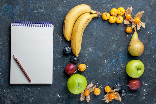 Top view yellow bananas with fresh green apples pears plums notepad and sweet cherries on the dark desk vitamine fruit berry health