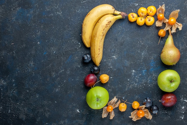 Вид сверху желтые бананы со свежими зелеными яблоками, грушами, сливами и черешней на темном столе, витамин, фрукты, ягоды, здоровье