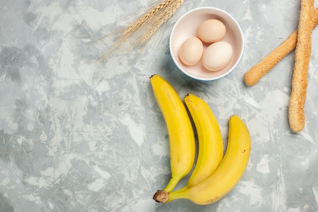 Banane gialle vista dall'alto con uova crude e pane panino sulla scrivania bianca leggera