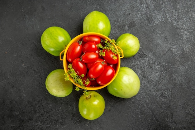 Top view yellow bucket filled with cherry tomatoes and dill flowers and rounded with green tomatoes on dark ground with copy space