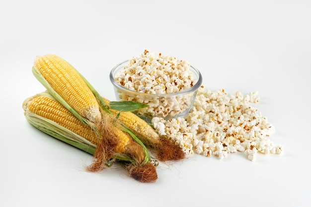 A top view yellow corns raw with green leaves and fresh popcorn on white desk, food meal color corn