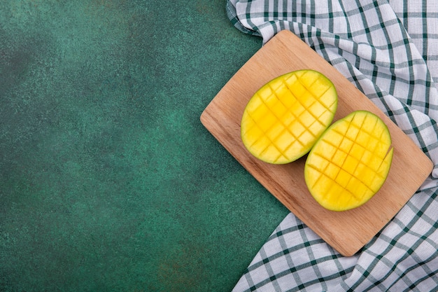 Free photo top view of yellow exotic fresh mango slices on a wooden kitchen board on checked tablecloth and green surface