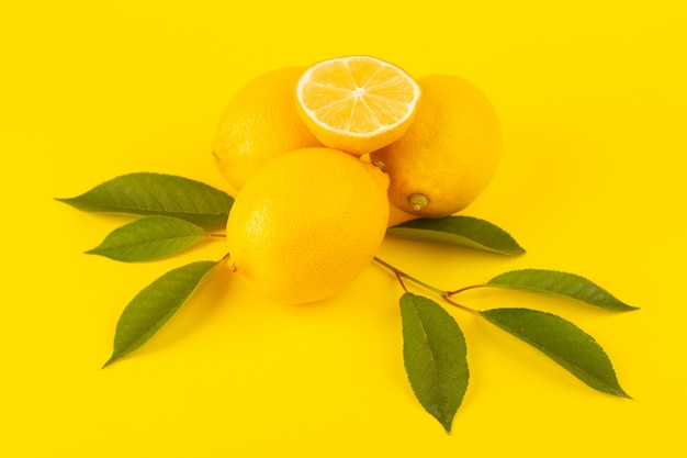 A top view yellow fresh lemons fresh ripe whole and sliced along with green leaves fruits isolated on the yellow background citrus fruit color