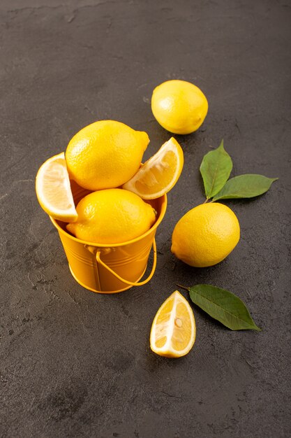 A top view yellow fresh lemons mellow and juicy whole and sliced inside yellow basket spread with green leaves on the dark background fruits citrus color