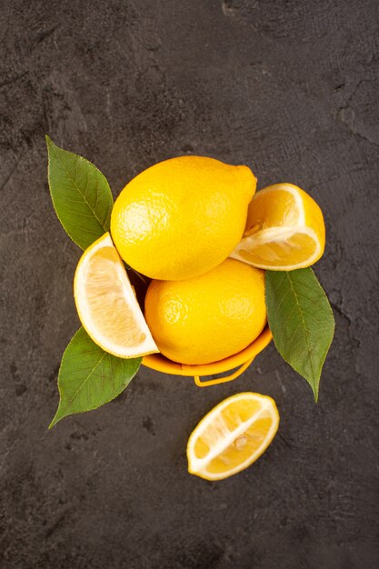 A top view yellow fresh lemons mellow and juicy whole and sliced inside yellow basket spread with green leaves on the dark background fruits citrus color