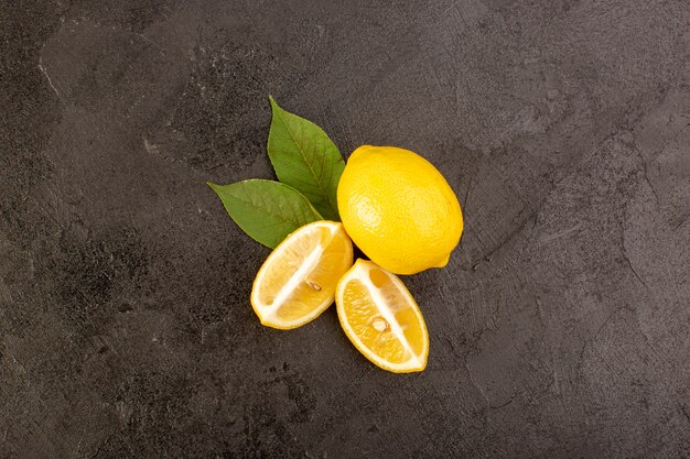 A top view yellow fresh lemons mellow and juicy whole and sliced with green leaves on the dark background fruits citrus color