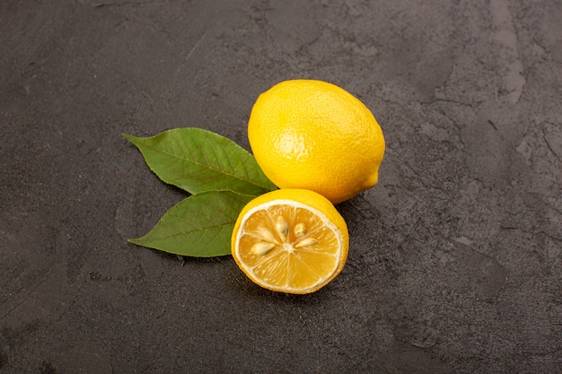 Вид сверху желтый свежий лимон сочный и сочный целый и нарезанный зелеными листьями на темном фоне фруктов цитрусового цвета