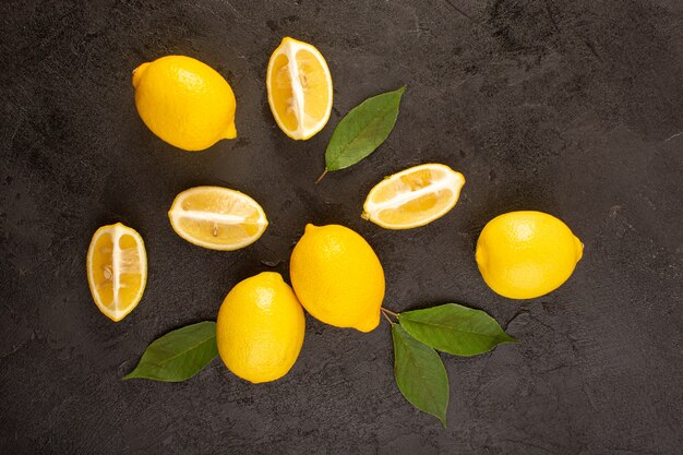 A top view yellow fresh lemons mellow and juicy whole and sliced with green leaves on the dark background fruits citrus color