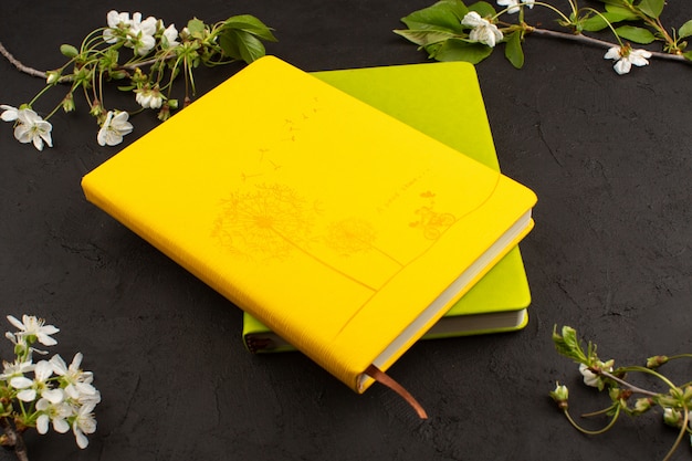 top view yellow green copybooks along with white flowers on the dark background