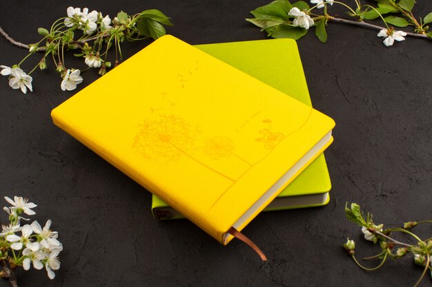 top view yellow green copybooks along with white flowers on the dark background