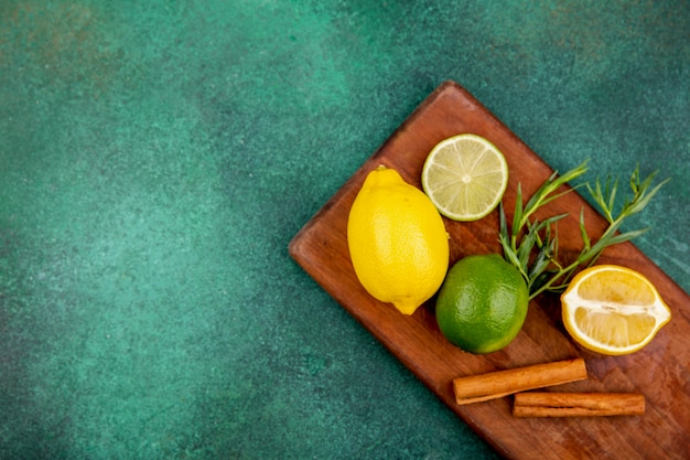 Top view of yellow and green lemons on a wooden kitchen board with cinnamon sticks on green surface