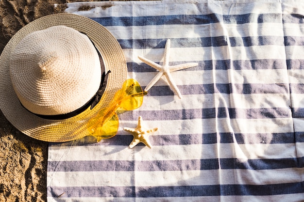 Top view of yellow heart sunglasses, straw hat and starfish on beach towel at beach