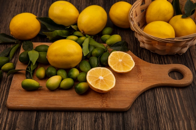 Top view of yellow lemons on a bucket with lemons and kinkans on a wooden kitchen board on a wooden surface