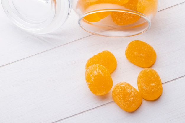 Top view of yellow marmalade candies scattered from a glass jar on white