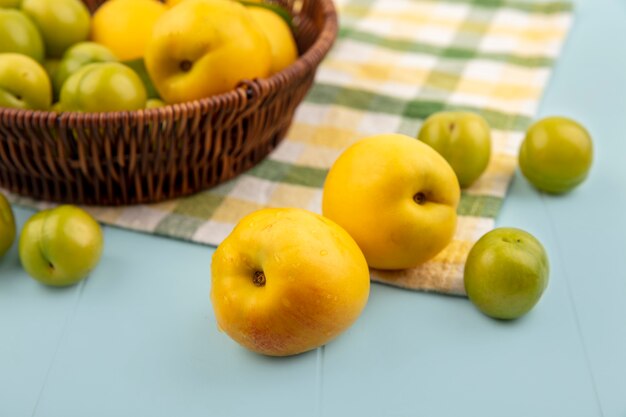 Top view of yellow peaches with green cherry plums on a checked tablecloth on a blue background