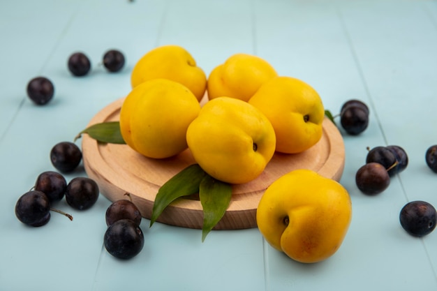 Free photo top view of yellow peaches on a wooden kitchen board with sour sloes isolated on a blue background