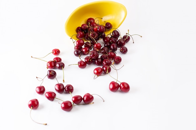 Piatto giallo di vista superiore con le ciliege rosse aspre fresche sul succo pastoso di colore della frutta del fondo bianco