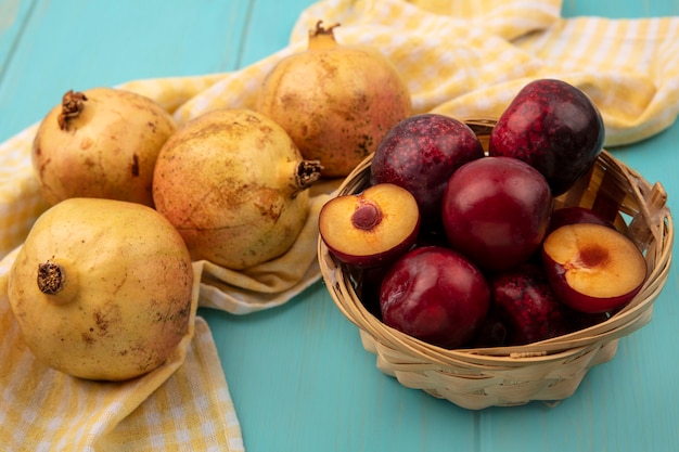 Top view of yellow pomegranates isolated on a yellow checked cloth with pluots on a bucket on a blue wooden surface