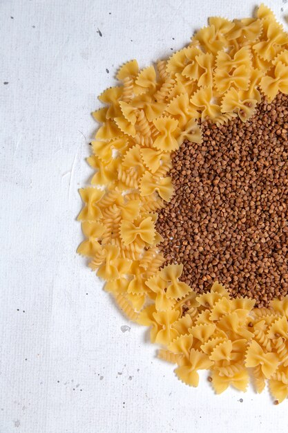 Top view yellow raw pasta little formed with buckwheat on the white desk pasta italy food meal