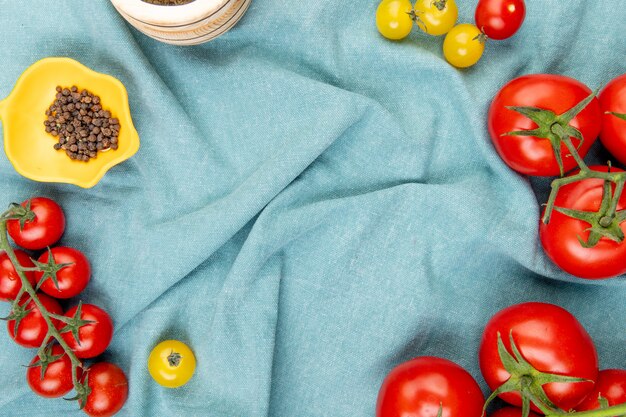 Top view of yellow and red tomatoes with black pepper seeds on blue cloth table 