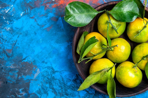 Top view yellow tangerines with leaves in wooden bowl on blue isolated surface free place