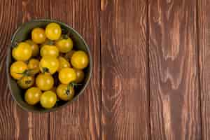 Free photo top view of yellow tomatoes in bowl on left side and wooden table