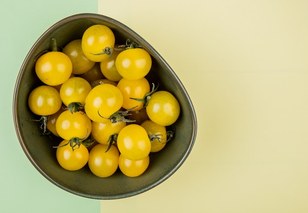 Top view of yellow tomatoes in bowl on yellow and green table 