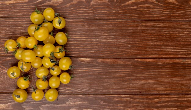 Top view of yellow tomatoes on left side and wooden table 