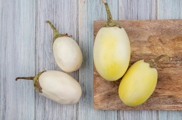 Top view of yellow and white eggplants on cutting board and on wooden background