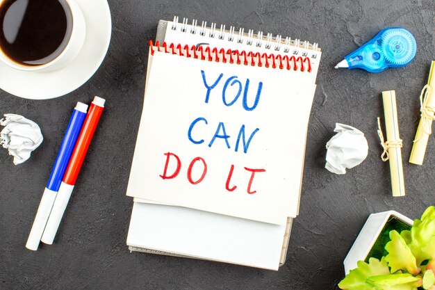 Top view you can doit written on notepad red and blue markers note papers cup of tea on black