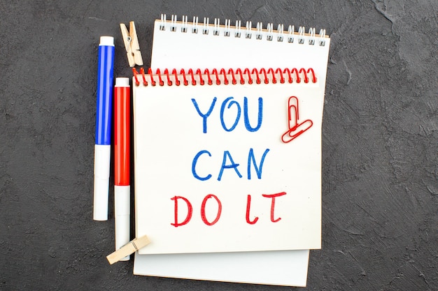 Free photo top view you can do it written on notepad red and blue markers clothespins gem clips on black table