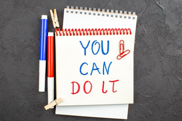 Top view you can do it written on notepad red and blue markers clothespins gem clips on black table