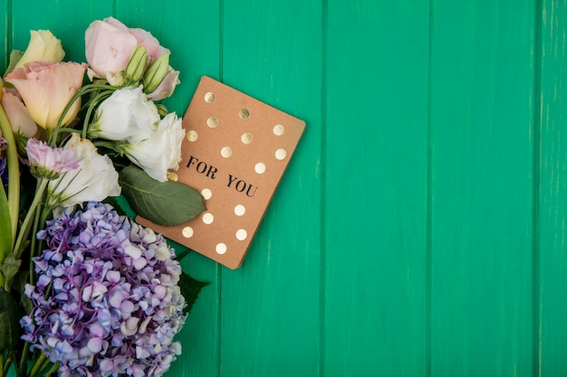 Top view of for you card and flowers on green background with copy space