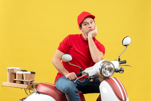 Top view of young adult wearing red blouse and hat delivering order in deep thoughts on yellow background