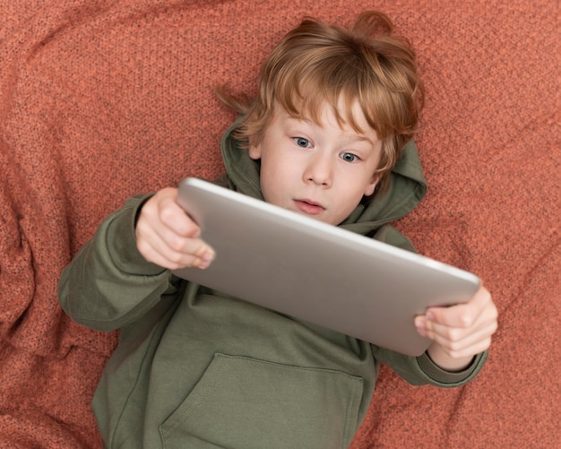 Free photo top view of young boy using tablet in bed