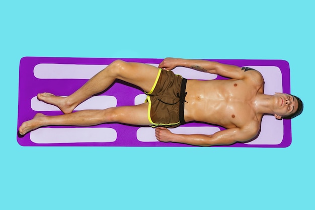 Top view of young caucasian male model's resting on beach resort on purple mat and blue