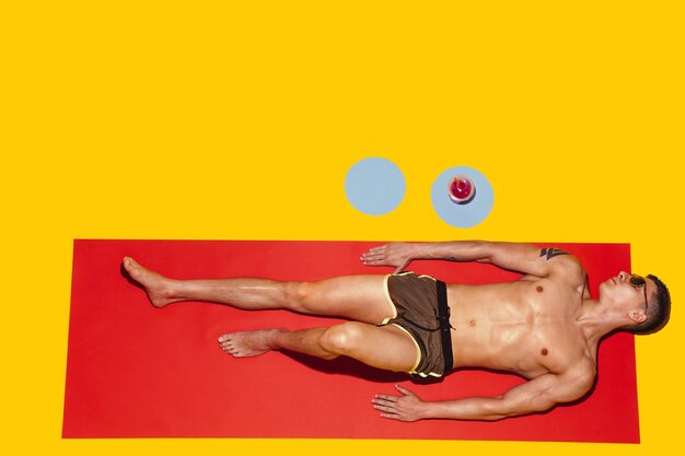 Top view of young caucasian male model's resting on beach resort on red mat and yellow