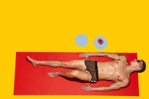 Top view of young caucasian male model's resting on beach resort on red mat and yellow
