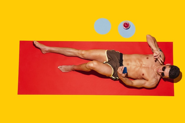 赤いマットと黄色のビーチリゾートで休んでいる若い白人男性モデルの上面図