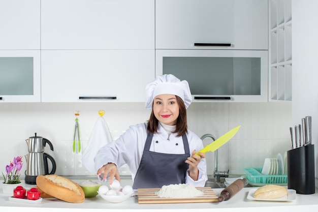 Top view of young concentrated female chef in uniform preparing food in the white kitchen