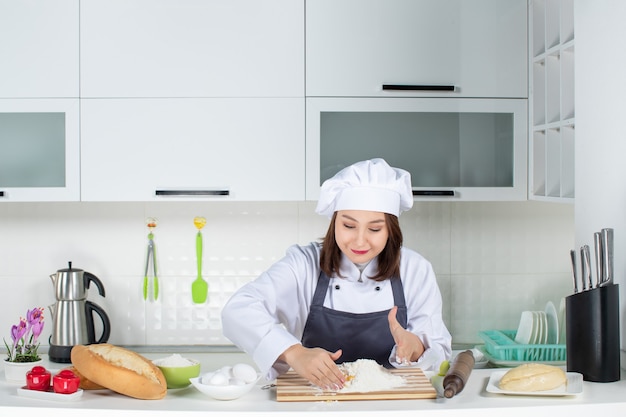 Top view of young concentrated female chef in uniform standing behind table cooking food in the white kitchen
