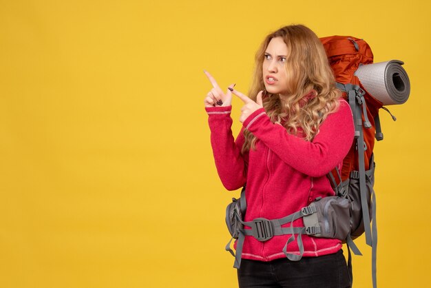 Вид сверху молодой сконцентрированной путешествующей девушки, собирающей свой багаж и указывающей вверх