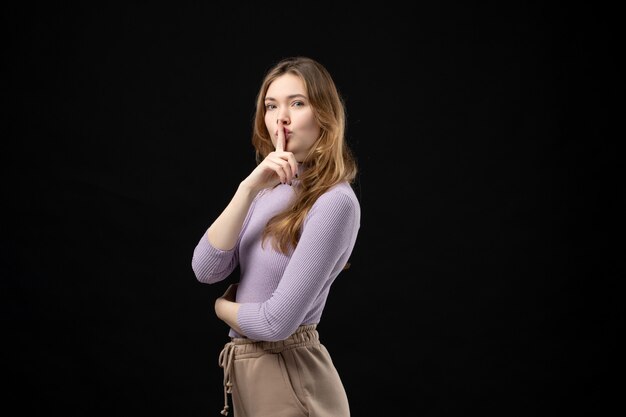 Top view of young confident girl making silence gesture on dark