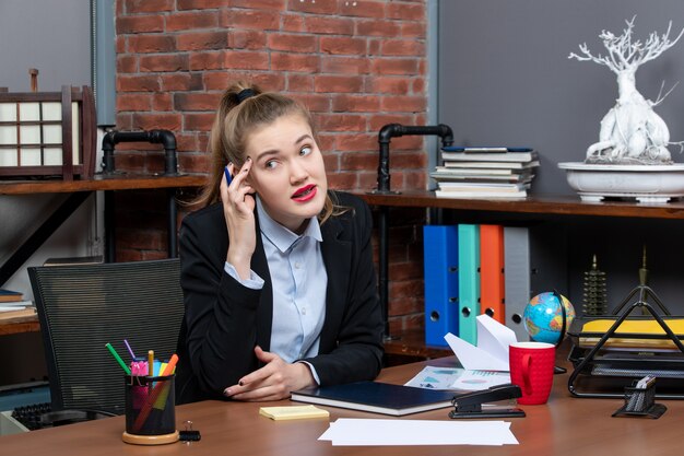 Top view of young exhausted female office worker sitting at her desk and posing for camera