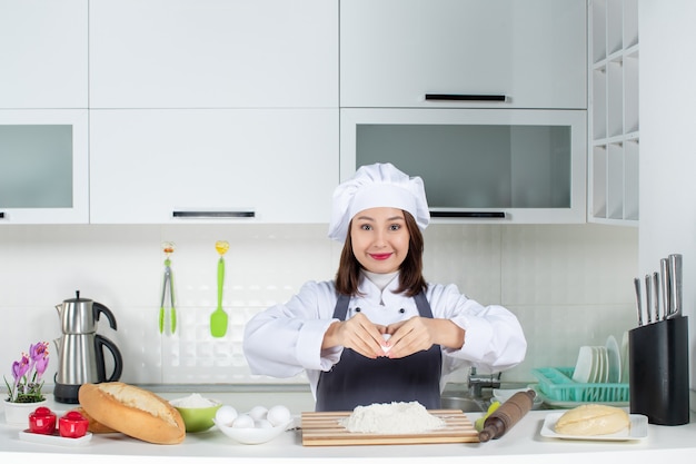白いキッチンで卵を食べ物に割ってテーブルの後ろに立っている制服を着た若い女性シェフの上面図