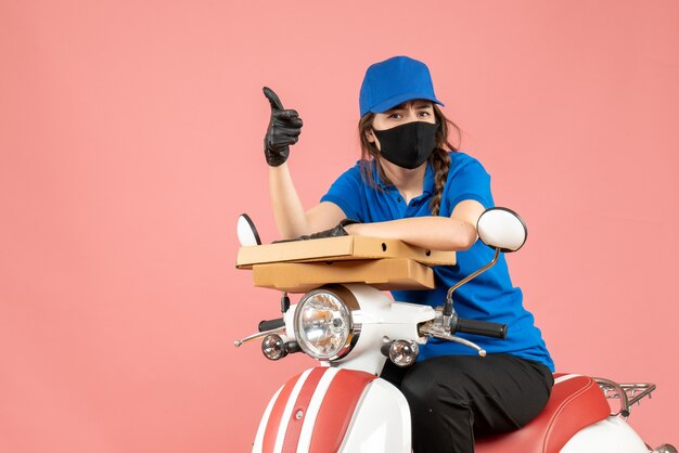 Top view of young female courier wearing medical mask and gloves sitting on scooter delivering orders asking something on pastel peach