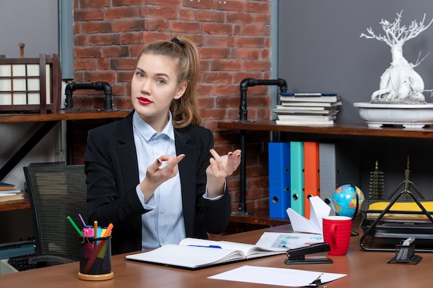 Free photo top view of young female sitting at a table and feeling curious about something in the office