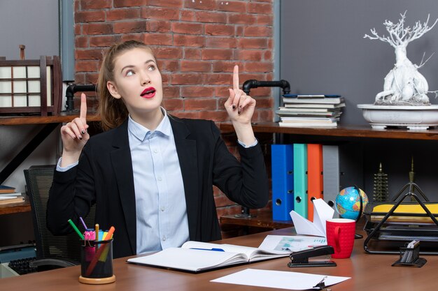 Top view of young female sitting at a table and pointing up in the office