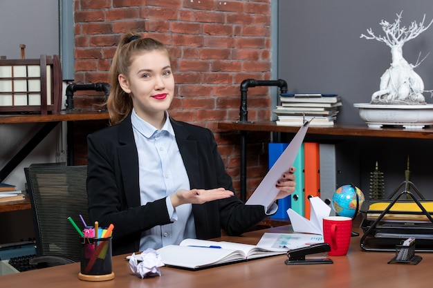 Free photo top view of young female sitting at a table and showing the document in the office